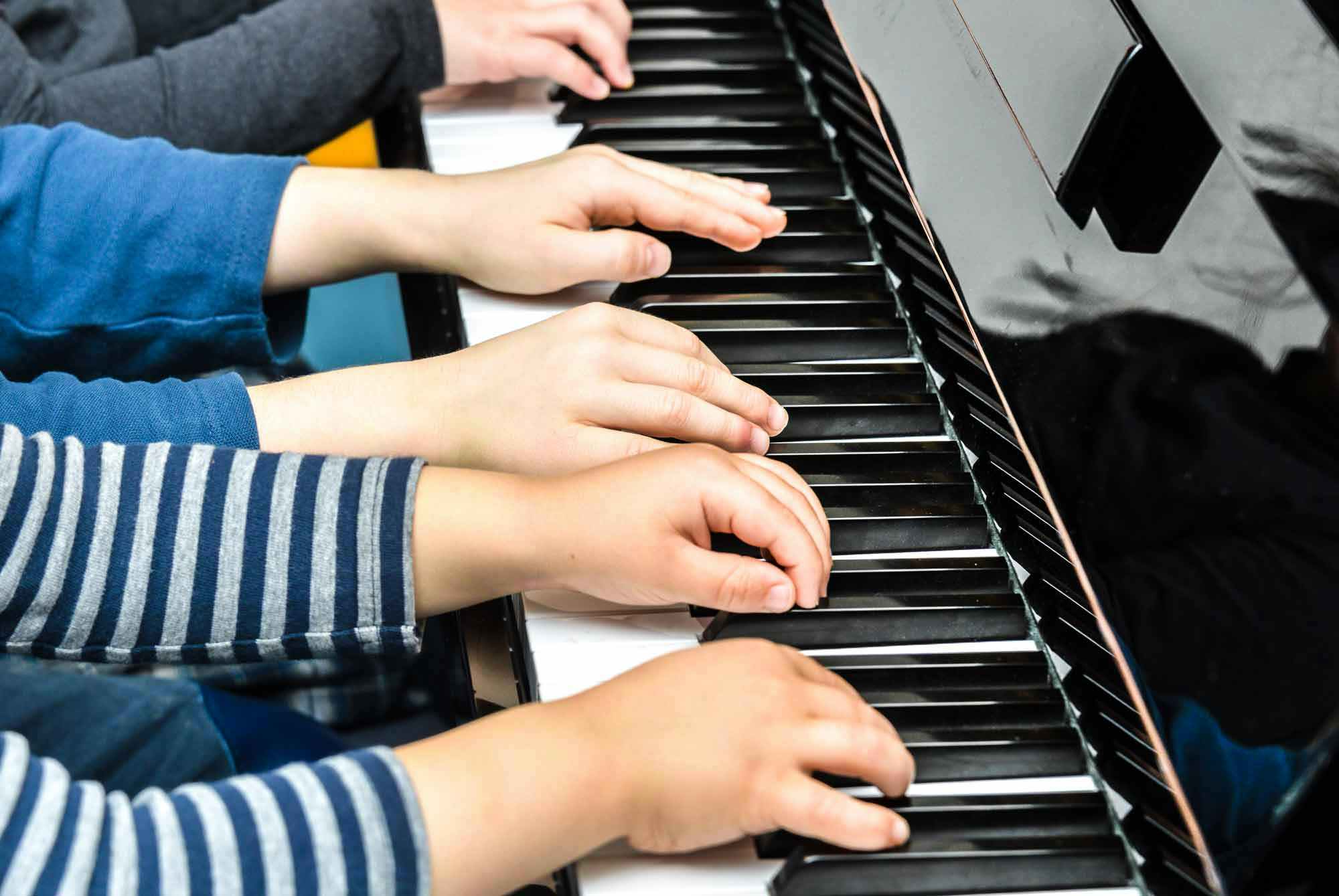Plusieurs mains d'enfants sur un même piano dans un cours de musique